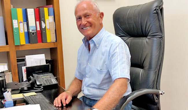 Alan d founder Alan Hemmings sitting at computer desk smiling.